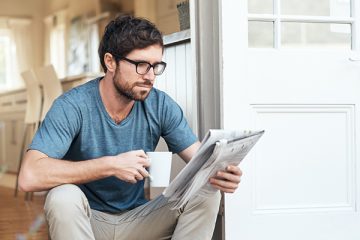 Mann liest auf der Veranda sitzend Zeitung