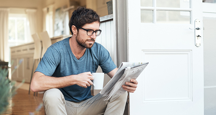 Mann liest auf der Veranda sitzend Zeitung