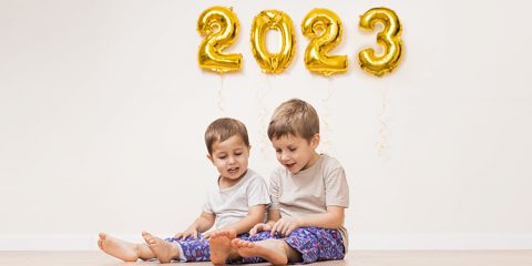 Glückliche Kinder sitzen auf Boden – an der Wand goldene Luftballons 2023