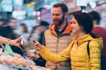 Junges Pärchen bezahlt per Handy via NFC-Technik auf dem Wochenmarkt