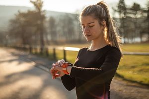 Junge Frau beim Joggen schaut auf ihre Smartwatch