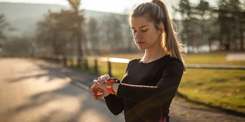 Junge Frau beim Joggen schaut auf ihre Smartwatch