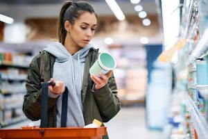 Junge Frau im Supermarkt prüft Angaben und Preis auf einem Produkt