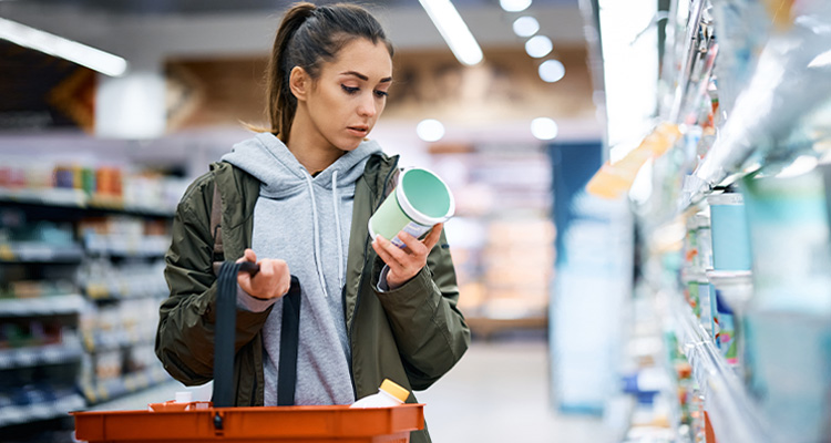 Junge Frau im Supermarkt prüft Angaben und Preis auf einem Produkt