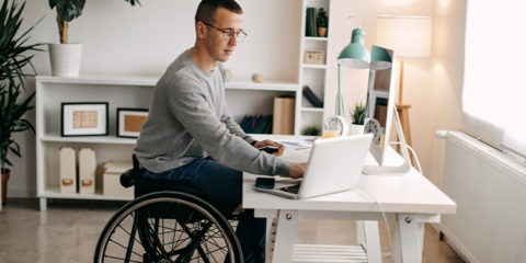 Barrierefrei wohnen – junger Mann im Rollstuhl sitzt am Schreibtisch