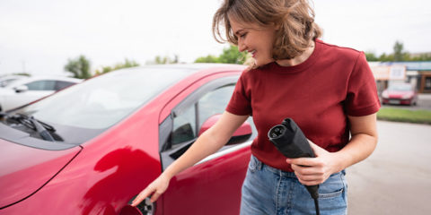E-Mobilität: Frau in roten T-shirt hält Stecker für Elektroauto