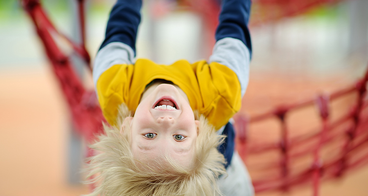 Blonder Junge hängt über Kopf an Spielgerät